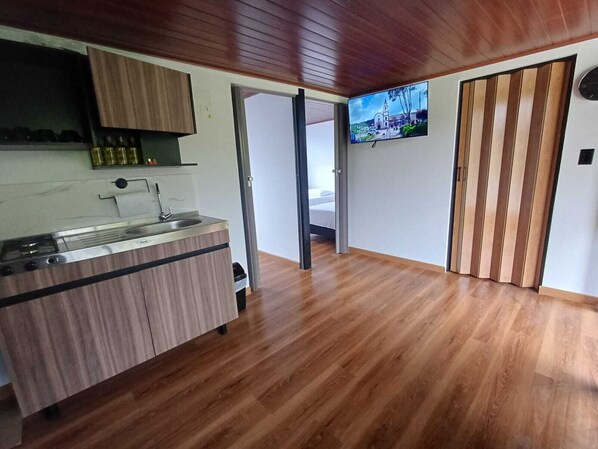 A modern kitchen with a built-in stove, a sink, and wooden cabinets. There is a television mounted on the wall and a sliding door leading to another room.