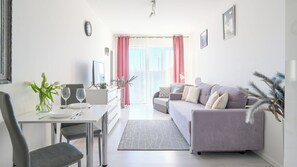 Ein modernes Wohnzimmer mit grauem Sofa, einem Esstisch mit Stühlen, einem Fernseher und einem Fenster mit Vorhängen.