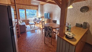 A cozy kitchen with a wooden table, chairs, a refrigerator, and a stone wall. - Cosy cocoon with mountain views (5 pers) at the foot of the slopes and paths (Le Grand-Bornand)