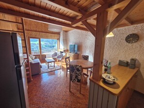 A cozy kitchen with a wooden table, chairs, a refrigerator, and a stone wall. - Cosy cocoon with mountain views (5 pers) at the foot of the slopes and paths (Le Grand-Bornand)