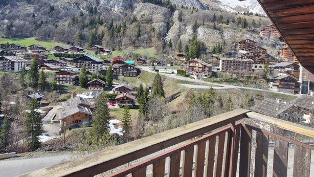 A mountain resort with chalet-style buildings, a winding road, and snow-capped peaks in the background. - Cosy cocoon with mountain views (5 pers) at the foot of the slopes and paths (Le Grand-Bornand)