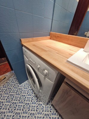 A laundry area with a washing machine, wooden countertop, and patterned floor tiles. - Cosy cocoon with mountain views (5 pers) at the foot of the slopes and paths (Le Grand-Bornand)
