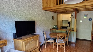 A living room with a TV, wooden furniture, a dining table, and a kitchen in the background. - Cosy cocoon with mountain views (5 pers) at the foot of the slopes and paths (Le Grand-Bornand)