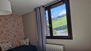 A bedroom with a bed, floral wallpaper, a window with a view of a green landscape and mountains, and a radiator. - Cosy cocoon with mountain views (5 pers) at the foot of the slopes and paths (Le Grand-Bornand)