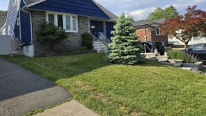 A residential house with a blue exterior, a brick foundation, and a small evergreen tree in the front yard.