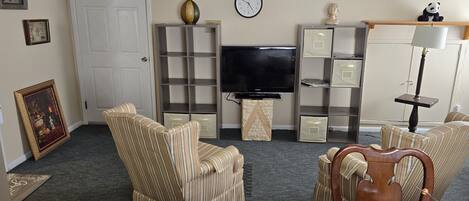 A living room with striped armchairs, a television, a clock, and a panda figurine.