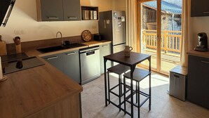 Una cocina moderna con vigas de madera, armarios grises, una encimera negra y una pequeña mesa con taburetes.