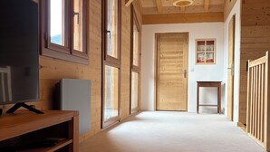 Una habitación amplia con paredes de madera y un techo alto, que incluye un televisor, una mesita pequeña y una escalera que conduce a otro nivel.