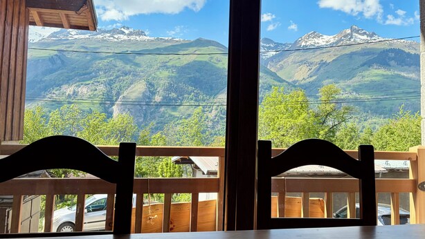Una mesa y sillas de madera en una habitación con ventanas grandes que dan a un paisaje montañoso.