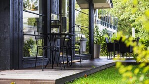 Een modern buiten zitgedeelte met een tafel, stoelen, grote ramen en uitzicht op groen.