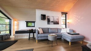 Een moderne woonkamer met een modulaire bank, een klein rond voetenbankje, een zwarte salontafel en een boekenkast.