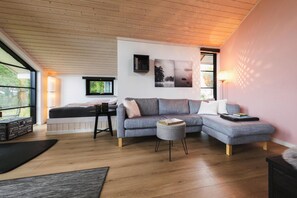 Ein modernes Wohnzimmer mit einer Eckcouch, einem kleinen runden Hocker, einem schwarzen Couchtisch und einem Bücherregal.