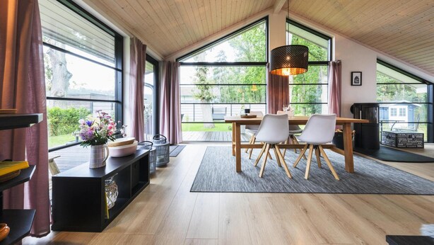Een ruime kamer met een hoge plafond, grote ramen, een eethoek met een tafel en stoelen, en een gezellige zithoek met een open haard.