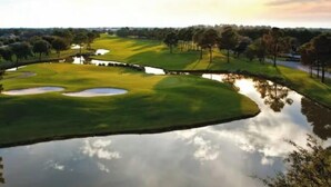 Ein Golfplatz mit Wasserhindernissen, Sandbunkern und blauem Himmel.