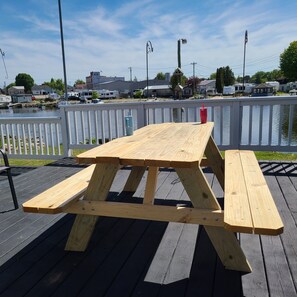 A wooden picnic table with benches on a deck by a lake. - Waterfront 4-Bedroom Home on Ahnapee River with Boat Dock/Slip, Garage, WiFi (Algoma)