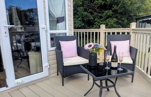 Eine Terrasse im Freien mit zwei Korbstühlen, einem Glastisch, einer Vase mit Blumen und zwei Weinflaschen.