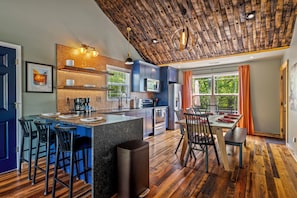 A modern kitchen with a bar area, wooden ceiling, and large windows.