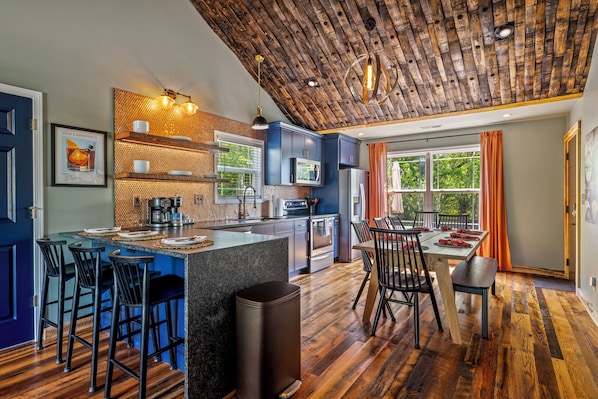 A modern kitchen with a bar area, wooden ceiling, and large windows.