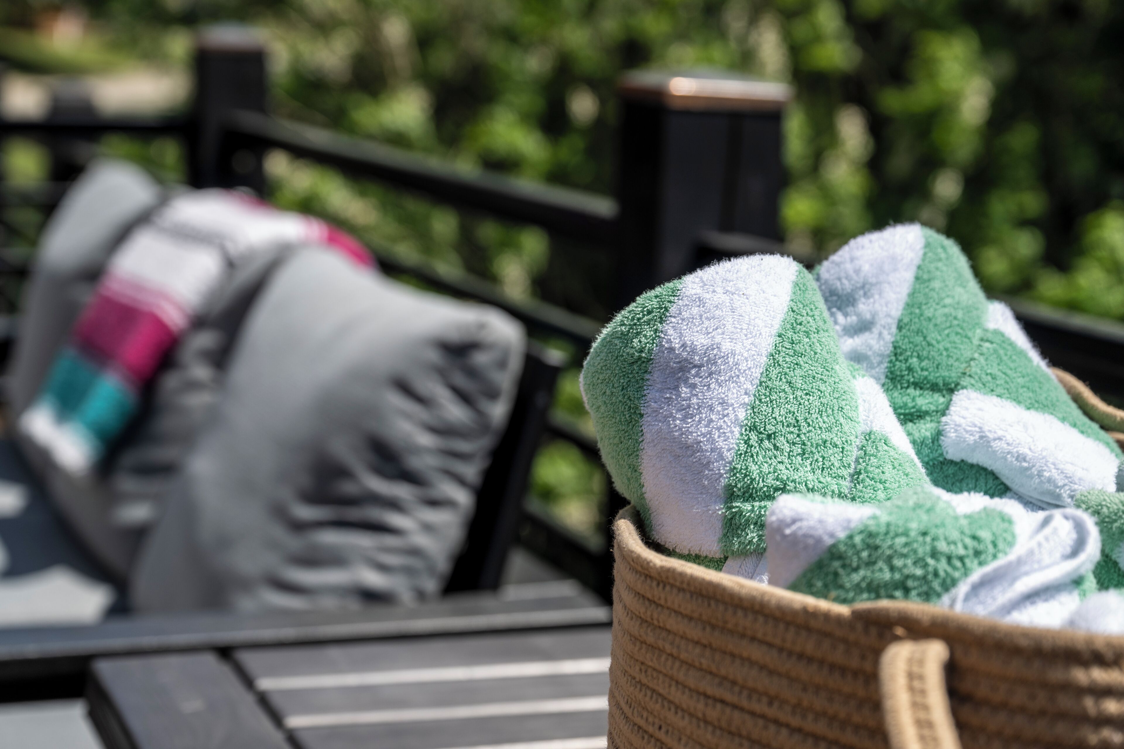 A wicker basket with green and white towels on a deck.