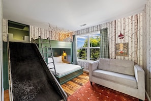 A room with a bunk bed, a sofa, a window with a view, and a wall with a birch tree pattern.