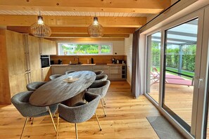 A modern kitchen with a dining area, wooden floors, and large windows. - Ferienhaus Nordwind mit Sauna am Dümmer See (Dümmer)