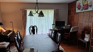 A dining area with a long table, chairs, a piano, a desk with a computer, and a window with curtains. - Charming 1-bedroom available in the house  Burlington perfect for a cozy getaway (Burlington)