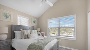 A bedroom with a bed, nightstand, window, ceiling fan, and artwork on the walls. - Marlin House -  Waterfront Pool Home Near Marina (Marathon)