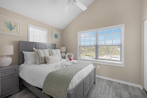 Ein Schlafzimmer mit Bett, Nachttisch, Fenster und Deckenventilator, außerdem Kunstwerken an den Wänden.