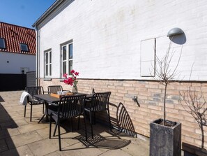 An outdoor patio with a table and chairs, a potted plant, and a wall-mounted light fixture. - 4 Star Holiday Home in Lokken (Lokken)