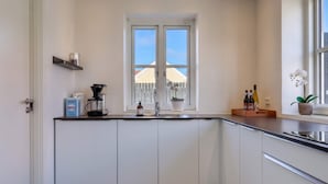 A modern kitchen with white cabinets, a coffee maker, a sink, and a window with a view of a fence and buildings. - 4 Star Holiday Home in Lokken (Lokken)