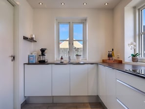 A modern kitchen with white cabinets, a coffee maker, a sink, and a window with a view of a fence and buildings. - 4 Star Holiday Home in Lokken (Lokken)