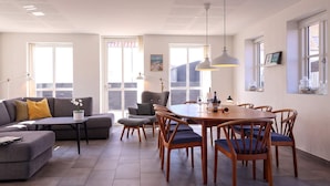 A modern living room with a sofa, a dining table with chairs, and a large window. - 4 Star Holiday Home in Lokken (Lokken)