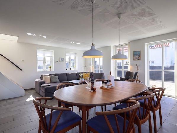A modern living room with a wooden dining table, blue chairs, a grey sofa, and large windows. - 4 Star Holiday Home in Lokken (Lokken)