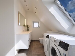 A modern bathroom with a skylight, a washing machine, and a toilet. - 4 Star Holiday Home in Lokken (Lokken)