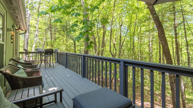 Eine Holterrasse mit Korbmöbeln und einem Tisch, mit Blick auf einen Wald.