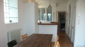 A dining area with a wooden table and chairs, a radiator, a window, and a kitchen in the background. - Renovated shop in the heart of La Rochelle (La Rochelle)