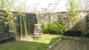 A wooden deck, a stone wall, and a wooden chair in a garden. - Renovated shop in the heart of La Rochelle (La Rochelle)