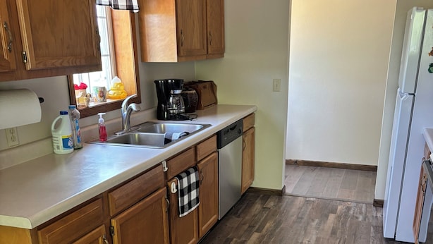 A kitchen with wooden cabinets, a dishwasher, a coffee maker, and a window with plaid curtains.