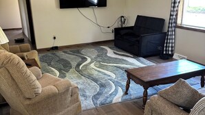 A living room with a flat-screen TV, a sofa, a coffee table, and a patterned rug.
