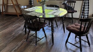 A dining area with a round table, four chairs, a vase with flowers, and a window with curtains.