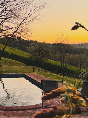 Eine friedliche Außenanlage mit Swimmingpool, einer Holzterrasse und Blick auf eine Hügellandschaft bei Sonnenuntergang.