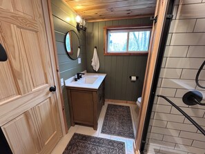 A bathroom with a wooden vanity, a mirror, a window, and a shower area.