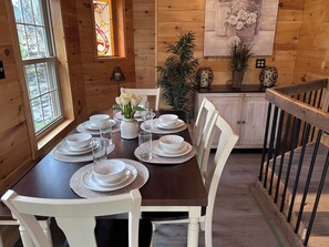 A wooden-paneled dining room with a table set for four, a stained glass window, and a painting on the wall.