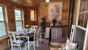 A wooden interior with a dining table set for four, white chairs, a staircase, and a 'WELCOME' sign.