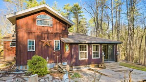 A rustic wooden house with a star decoration, stone pathway, and a forested backdrop.