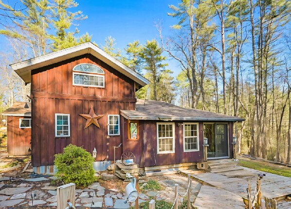 A rustic wooden house with a star decoration, stone pathway, and a forested backdrop.