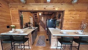A wooden interior with a kitchen and dining area, featuring a central island, chairs, and a rug.