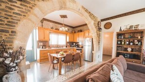 A rustic kitchen with wooden cabinets, a dining table, and a refrigerator. - Unique Villa Pietra: Priv. Pool Oasis, Top Beaches (ΡΟΔΟΣ)