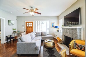 Ein Wohnzimmer mit Ecksofa, Kamin, Deckenventilator und einem großen, an der Wand montierten Fernseher.