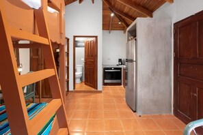 Eine Küche mit Kühlschrank, Herd und Spüle. Eine Holztreppe führt zu einer Schlafgalerie mit einem Etagenbett.